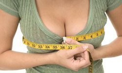 Picture of a woman, happy with her perfect breast reduction procedure she had at Top Plastic Surgeons in beautiful San Jose, Costa Rica.  The woman is facing the camera, measuring her breasts with a tape measure,  and wearing an olive colored blouse
