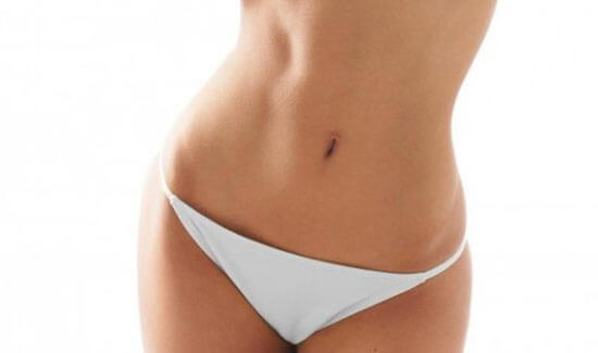 Picture of a woman facing the camera and happy with the perfect abdomen and waist liposuction procedure she had at Top Plastic Surgeons in beautiful San Jose, Costa Rica.  She is wearing a two piece bikini and showing a flat abdomen to the camera.